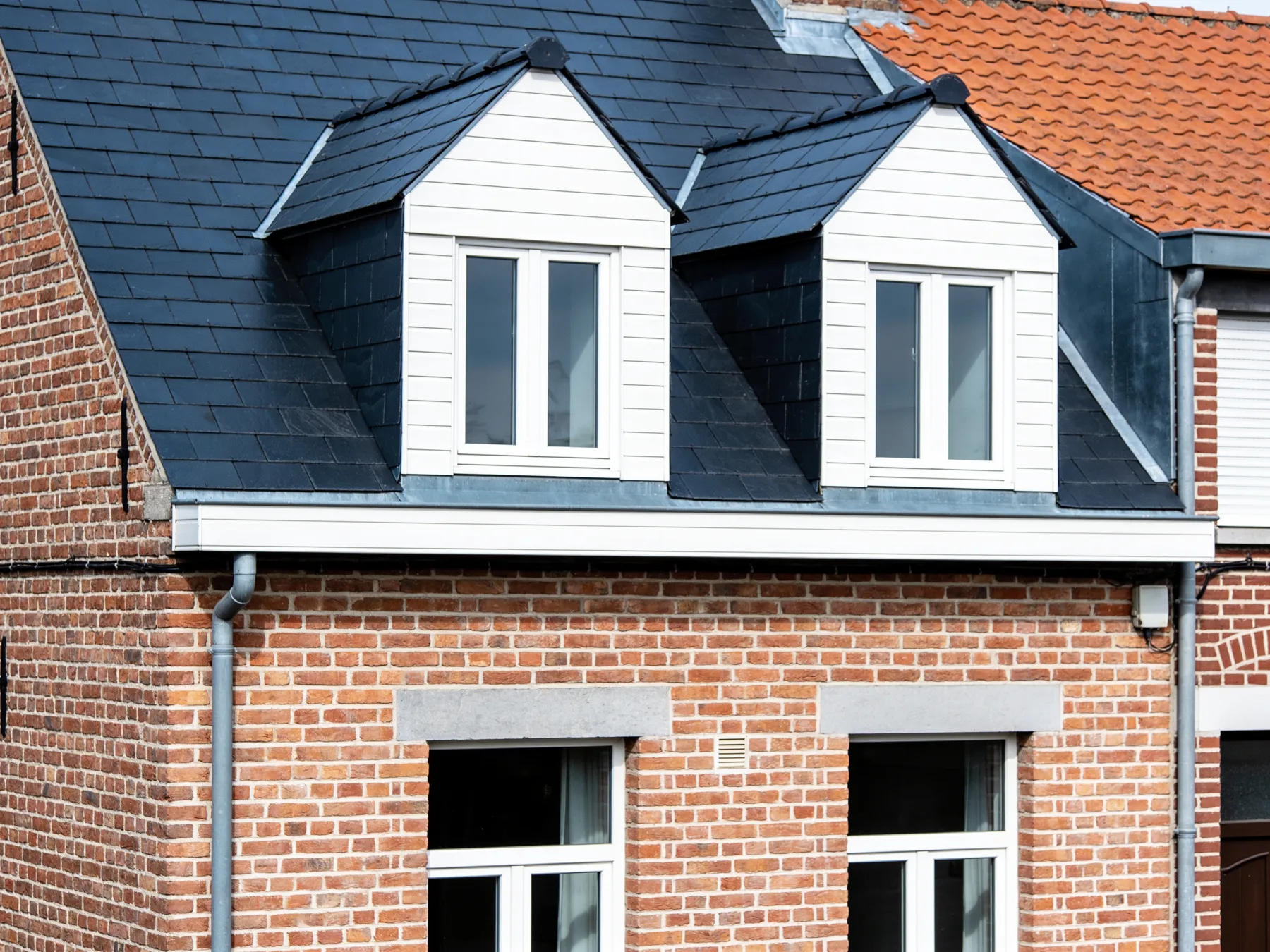 Afgewerkt hellend dak in natuurleien met twee witte dakkapellen op een gerenoveerde rijwoning