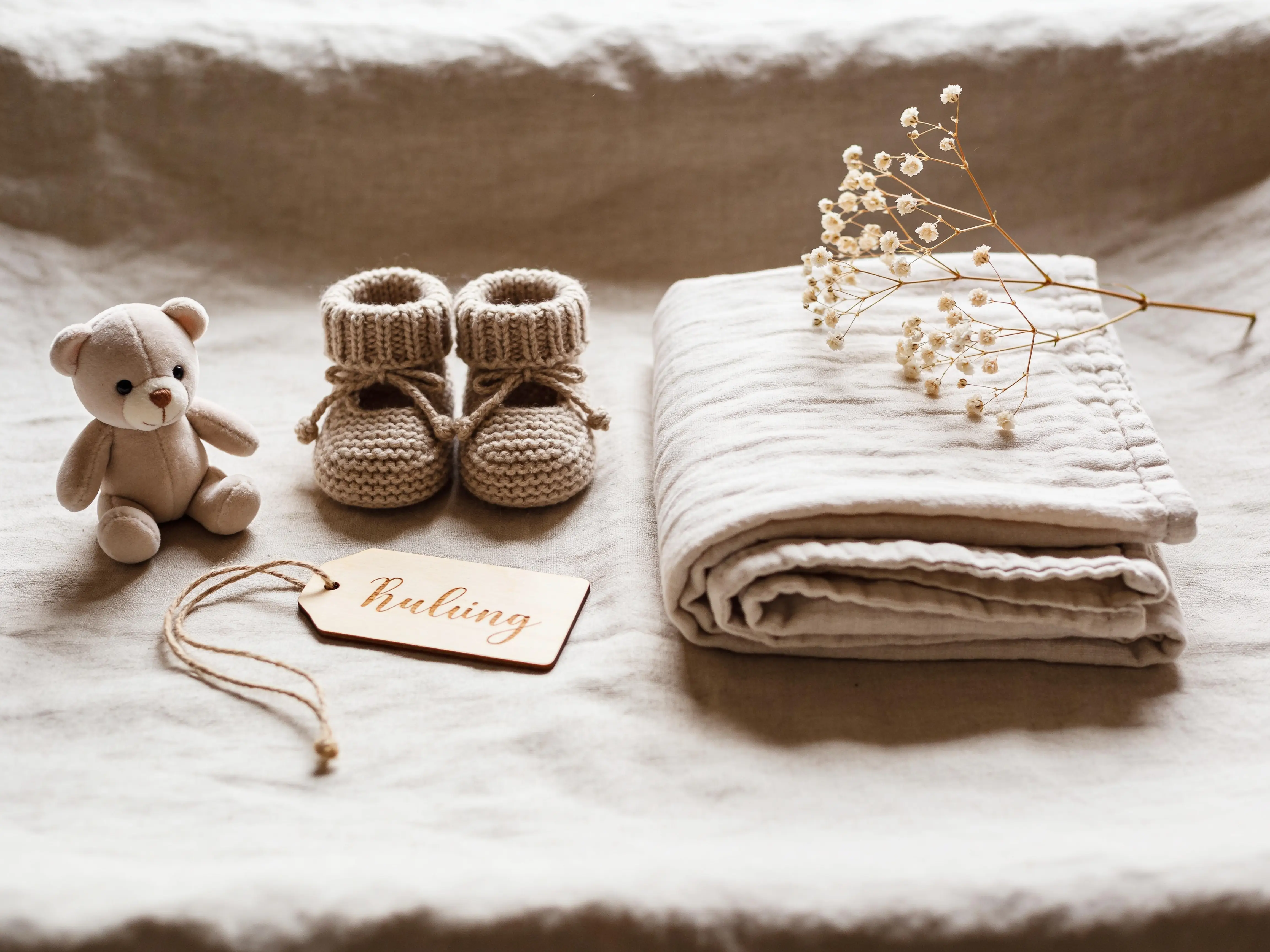 Newborn-details: gebreide slofjes, swaddle en droogbloemen op linnen